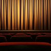 Theatersaal mit roten Sesselreihen vor geschlossenem Vorhang